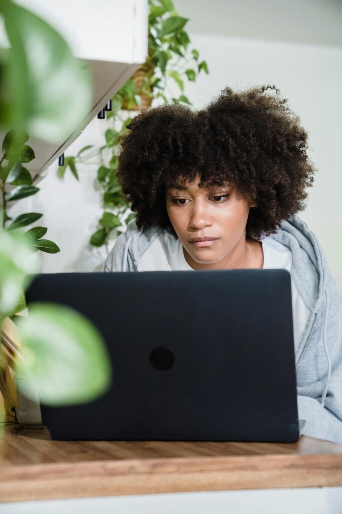 A woman concentrating on her laptop in a bright, plant-filled indoor space, embodying modern technology use.